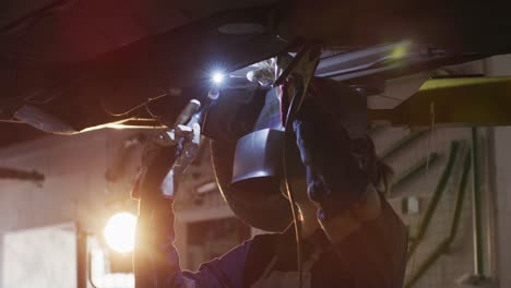 female mechanic wearing welding helmet welding under a car at a car service station