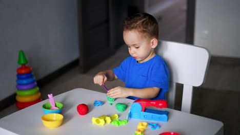 concentrated caucasian baby boy sitting at desk busy with a game. toddler plays with plasticine using a stick.