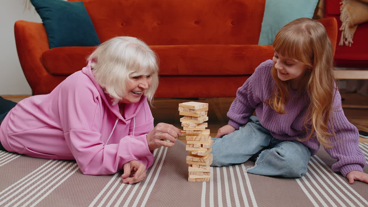 Excited little cute girl granddaughter playing building block game with smiling senior grandmother