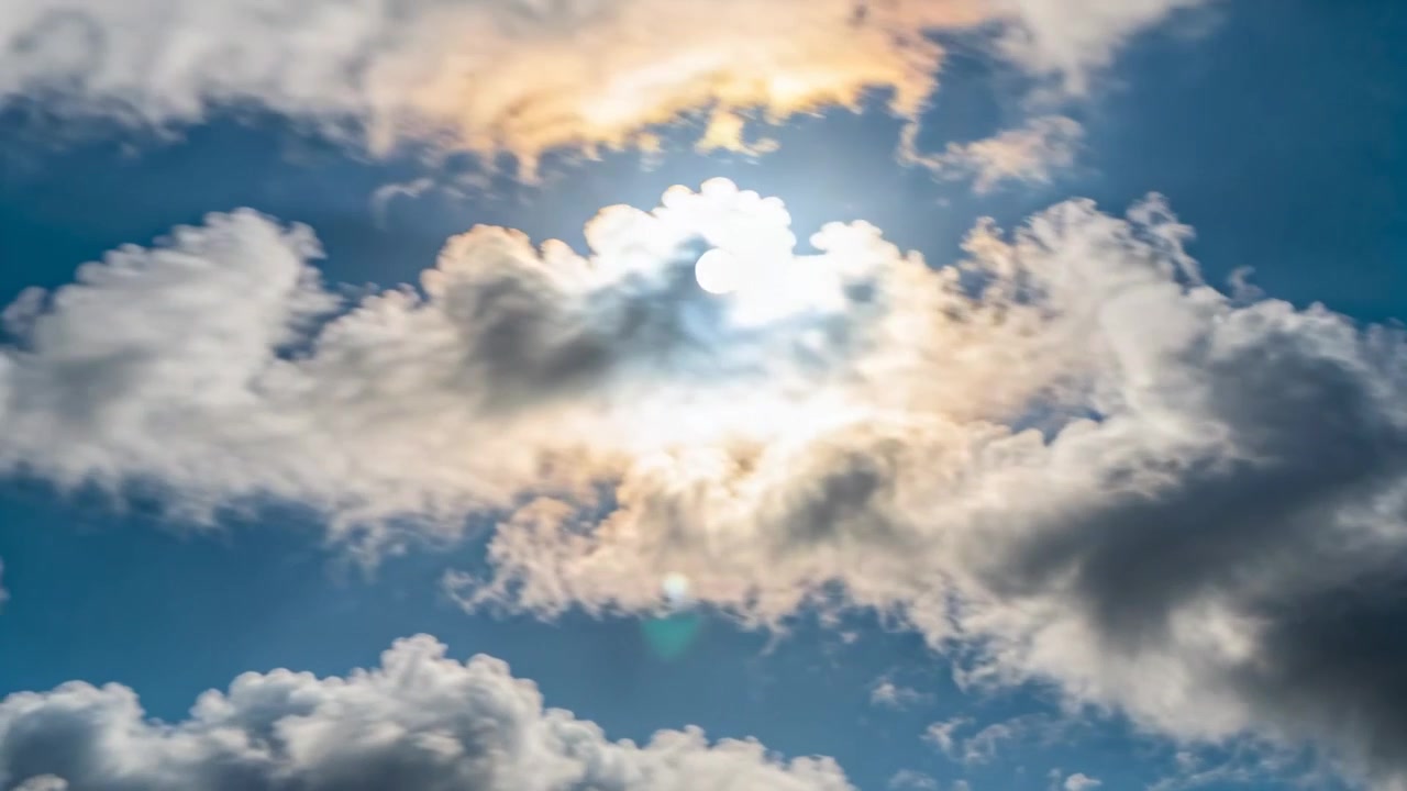 Brezza che sposta una grande nuvola cumuliforme che galleggia nel cielo blu, rivelando un alone solare e un bagliore dell'obiettivo