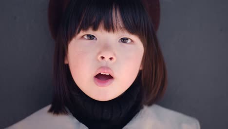 회색 코트와 모자를 입은 한국 소녀는 가게의 유리 문에서 봄에 거리에 서 있습니다.