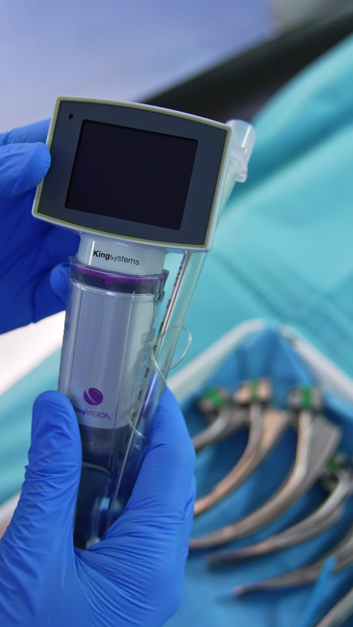Gloved hands of a medic holding a portable video laryngoscope. Doctor presses the button and little screen switches on. Close up. Vertical video