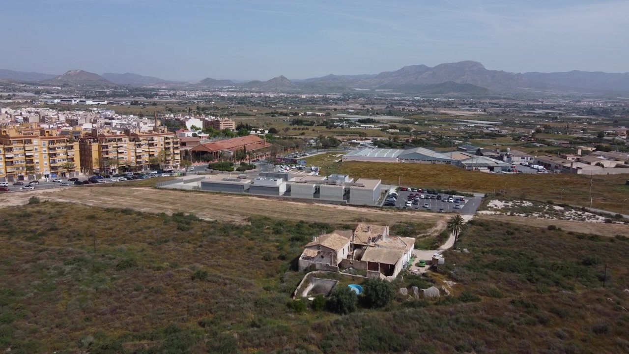 High-angle aerial drone shot zooming in on the medical health center in Aspe, Spain. Building surrounded by vacant lots and arid terrain. Public healthcare and regional infrastructure concept.