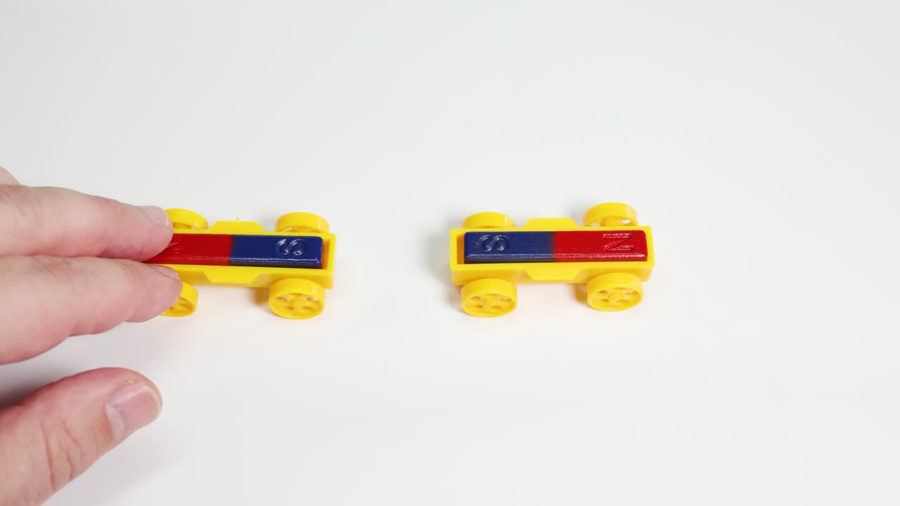 Hands manipulate toy cars with magnets, illustrating attraction and repulsion on a white surface under bright lighting