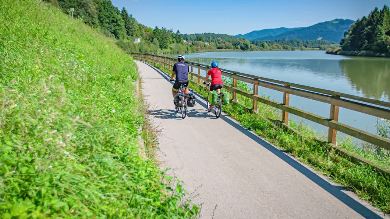 Wide angle left side panning shot of a man and women cycling along the beautiful Drava cycling Route in Muta Slovenia during the day