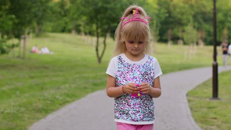 mädchen spielt mit pop-it-sensor-anti-stress-hand-spinner-squishy-blasen-spielzeug, während sie im park spazieren geht