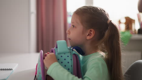 serious girl opens schoolbag with zippers sitting at desk