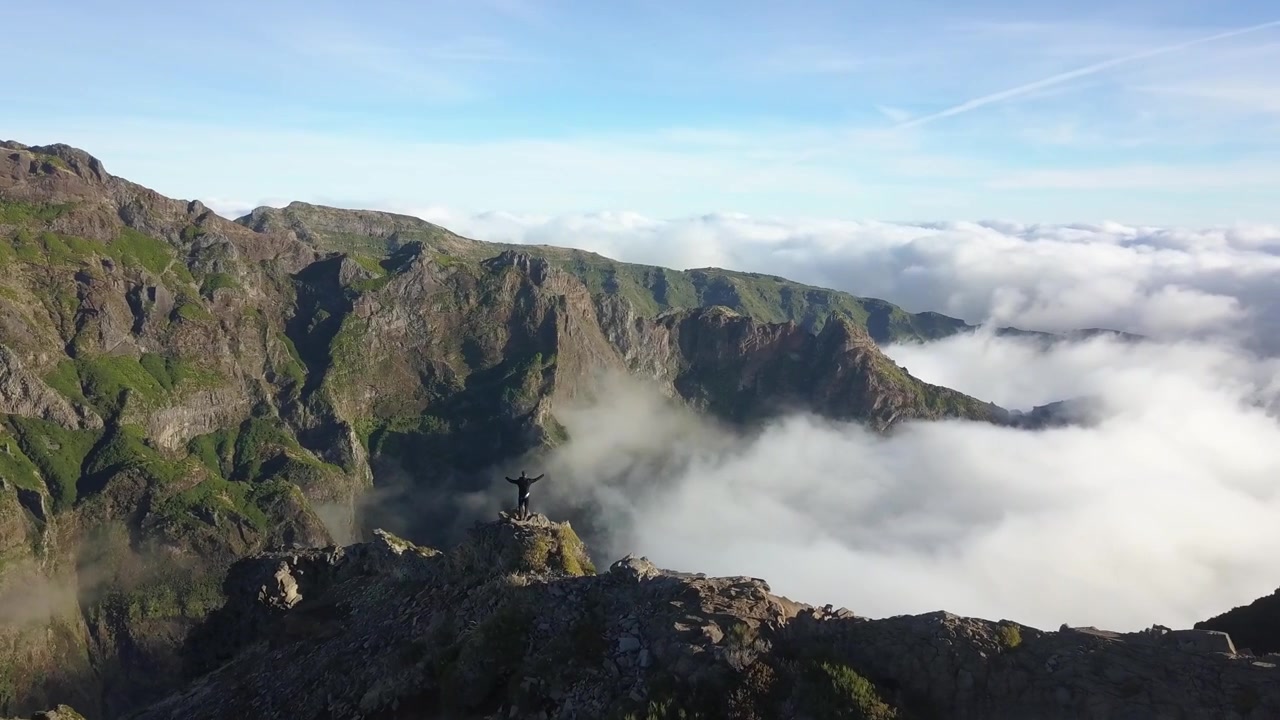 Splendida ripresa grandangolare con drone di un singolo escursionista che percorre un drammatico sentiero su cresta montuosa vulcanica a Madeira, Portogallo. Caratterizzato da imponenti cime rocciose, valli profonde e un'ampia luce mattutina