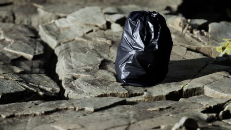 black trash bag lay on a rocky beach