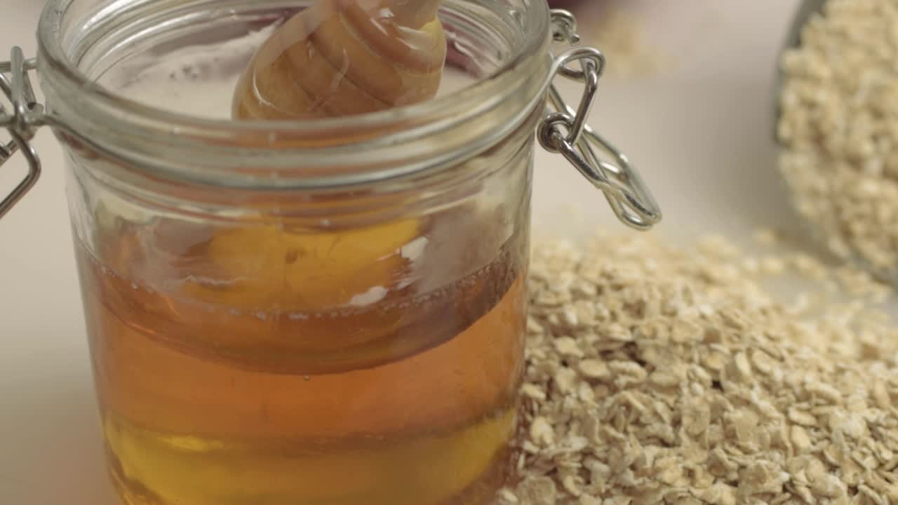 Stirring pot of golden runny honey with scoop of oats close up