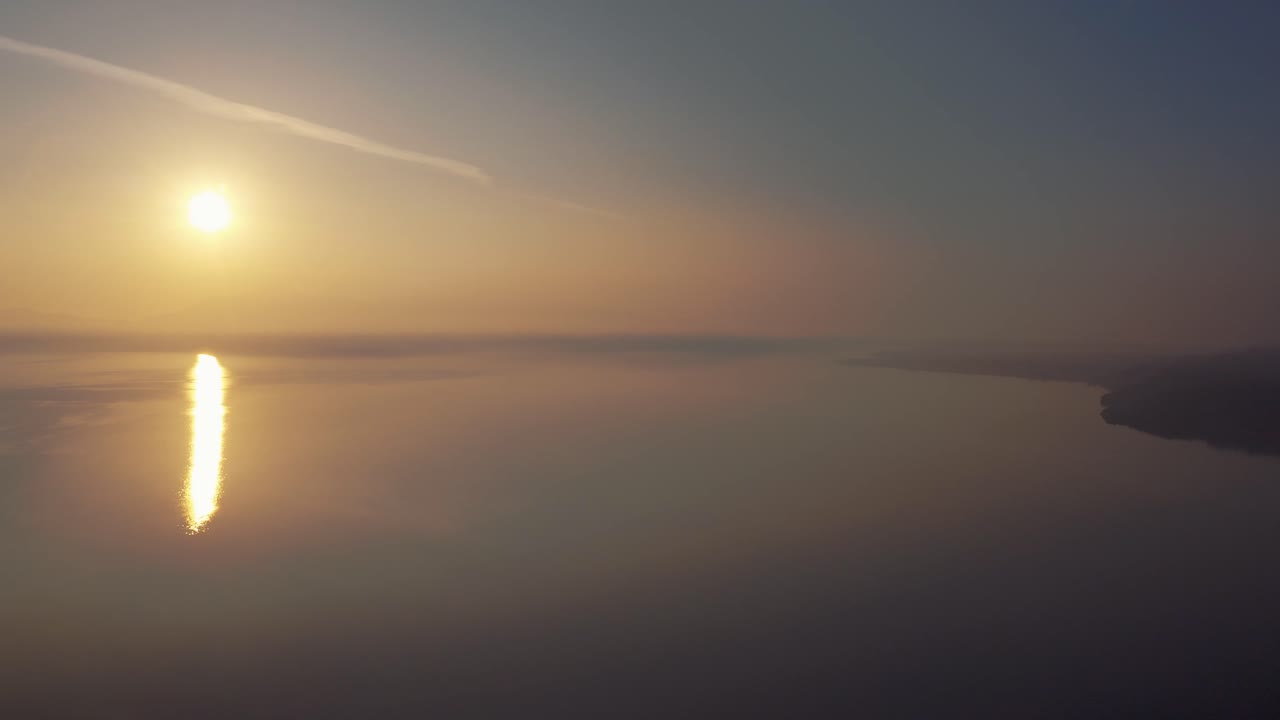 Drone flying above a misty sea coast on golden hour sunset, bird flying over hazy water surface in Lesvos, Greece.