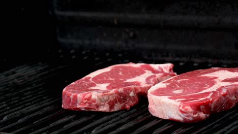 two raw rib-eye steaks getting ready to cook on a grill