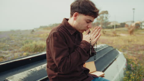man praying with a rosary and eyes closed on the shore during winter