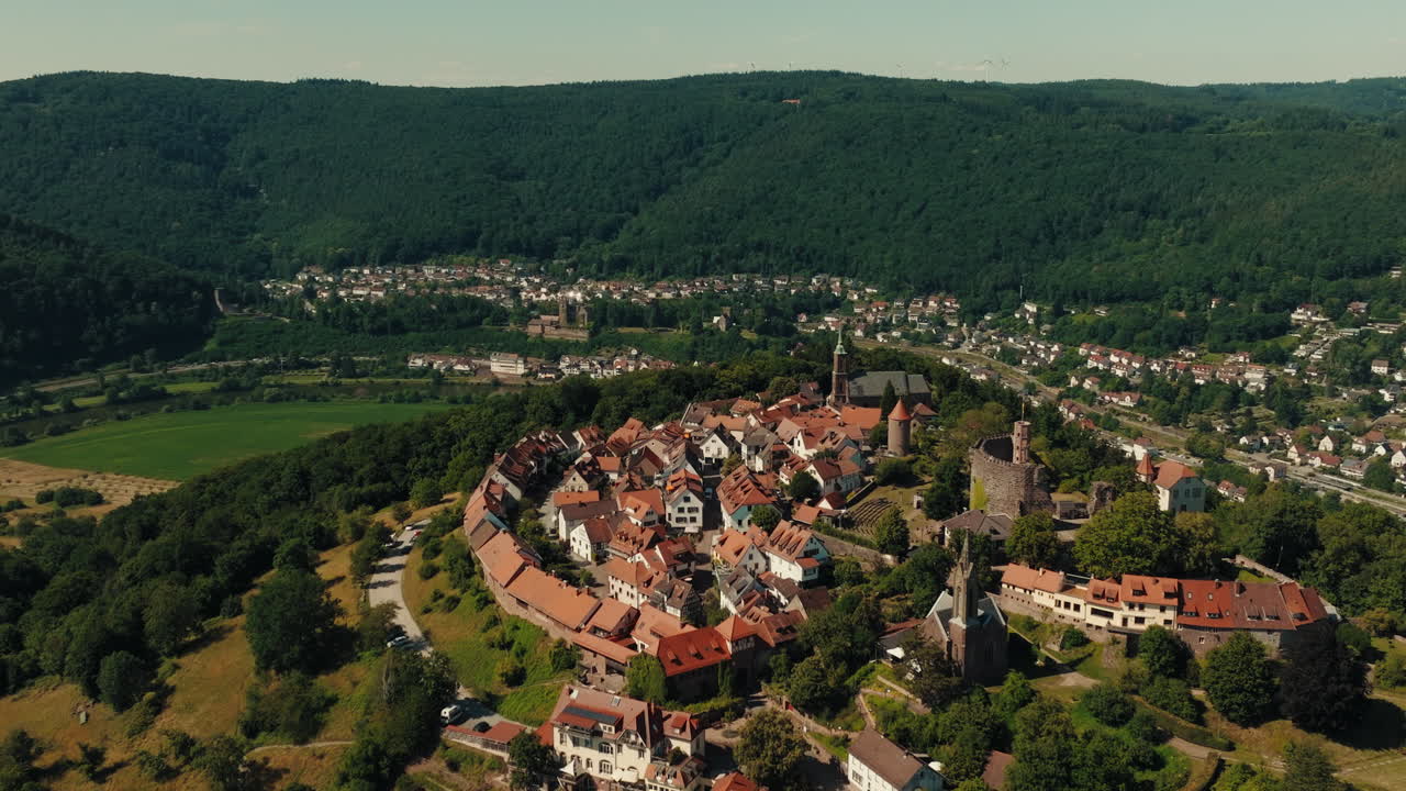 Aerial helix shot of mountaintop settlement with wide view of houses in Odenwald valley surrounded by green mountains
