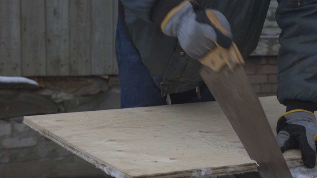 Un uomo con i guanti sta tagliando la linea marcata su una tavola di legno.