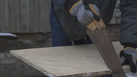 a man wearing gloves is cutting the marked line on the wood plank