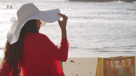 pretty latin brunette girl sat on caribbean beach with sunhat looks back with sexy smile