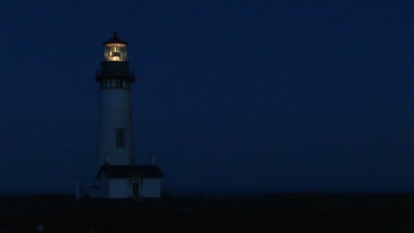 medium shot of lighthouse at night with its bright beacon signaling a warning to passing ships