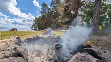 Young-woman-sitting-in-camping-by-campfire-smoke-pit,-in-nature-near-forest