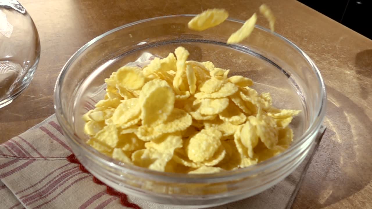 Knusprige gelbe Cornflakes in die Schale für ein köstliches Frühstück mit Milch am Morgen. Zeitlupe mit rotierender Kamerafahrt