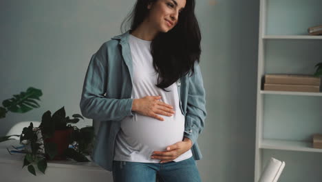 joven embarazada feliz mujer de negocios masajeando y acariciando su vientre en casa
