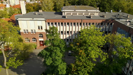 Faculty-of-Management-University-of-Gdansk,-old-building-in-historical-architecture-from-red-brick-and-green-tall-tree-on-parking