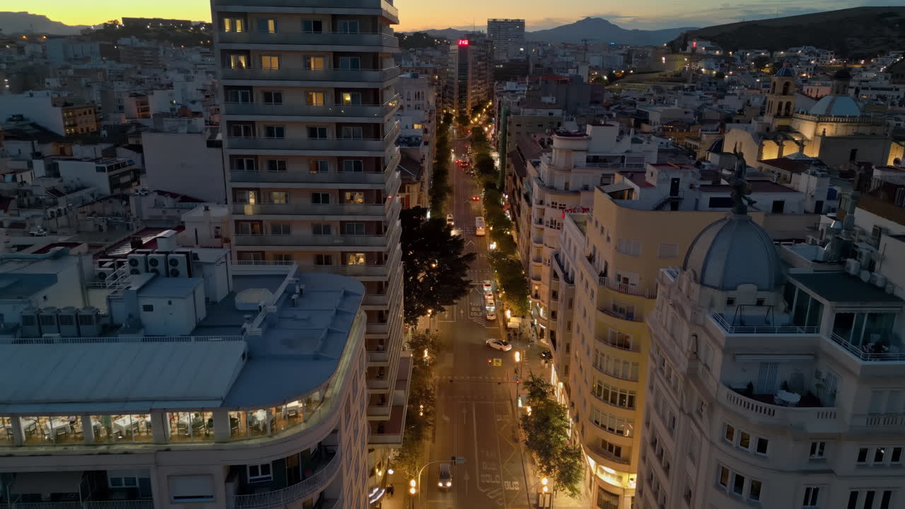 Aerial drone view of cars moving between the buildings in Alicante, Spain at sunset
