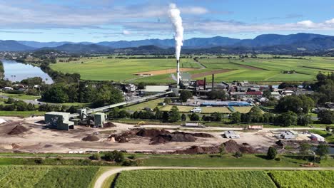 Drone footage captures a sugar mill surrounded by lush fields and mountains under clear skies in Murwillumbah, NSW
