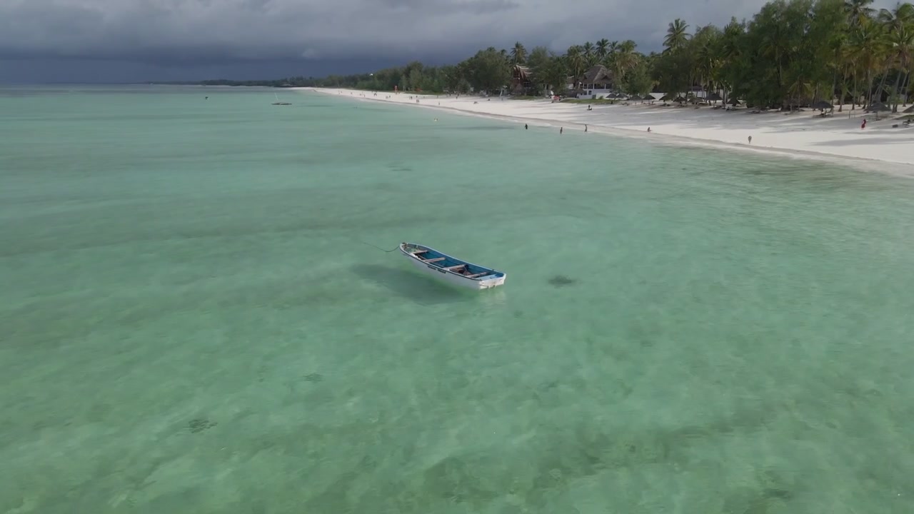Tanzanya, Zanzibar'daki Paje kıyısı açıklarında denizde geleneksel bir tekneye odaklanan bir video. Drone, tekneyi çekimin ortasında tutarak etrafında dönüyor ve sahili gözler önüne seriyor