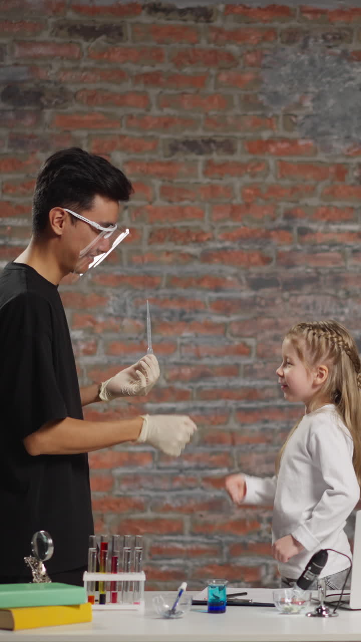Asian chemistry teacher and happy blonde little girl play rock paper scissors before experiment starting at fun science lesson in classroom