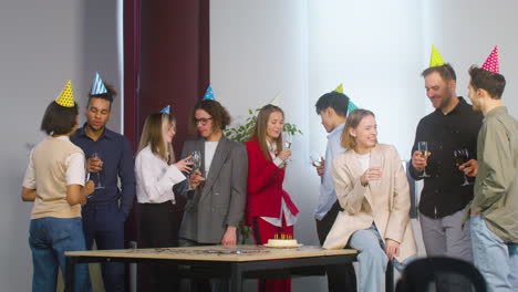 group of multiethnic colleague with party hat spending time together, drinking and talking at the birthday party in the office