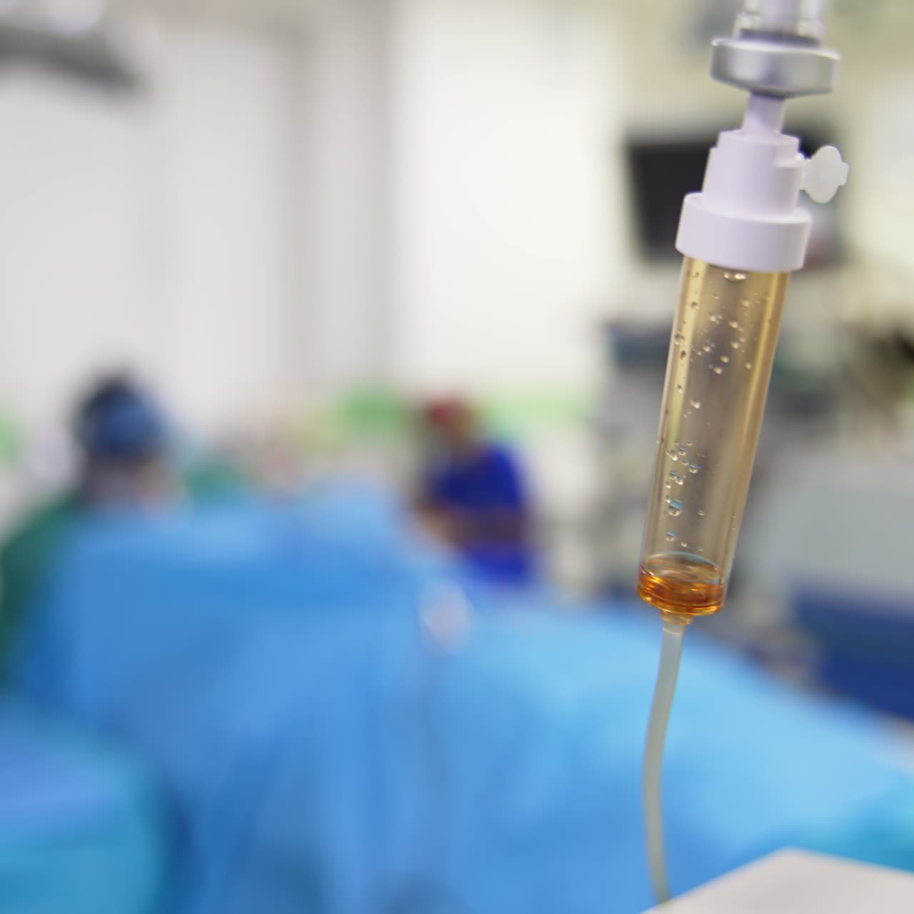 Drops falling in the drop counter in surgery theatre. Medical team working in the surgery room at backdrop in blur