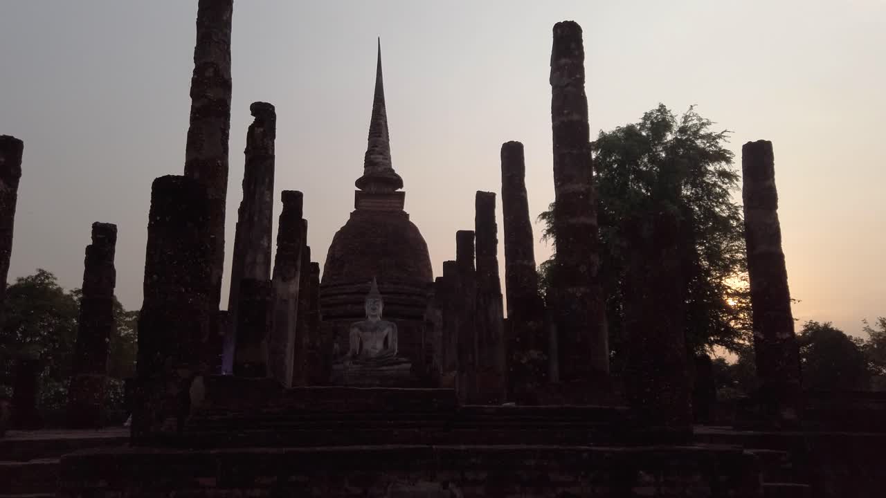 empuje hacia la gran estatua de buda sentada entre las ruinas históricas de la columna de piedra en la atracción del sitio del jardín religioso en sukhothai, tailandia