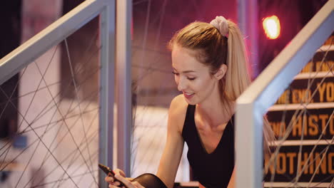 Beautiful-Female-Athlete-Text-Messaging-Through-Mobile-Phone-During-Break-At-Health-Studio-2