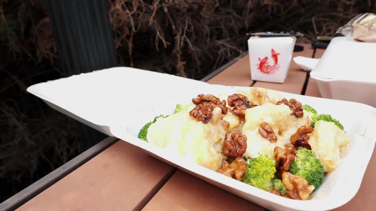 primer plano de comer camarones de nuez de miel con brócoli en un recipiente para llevar con palillos