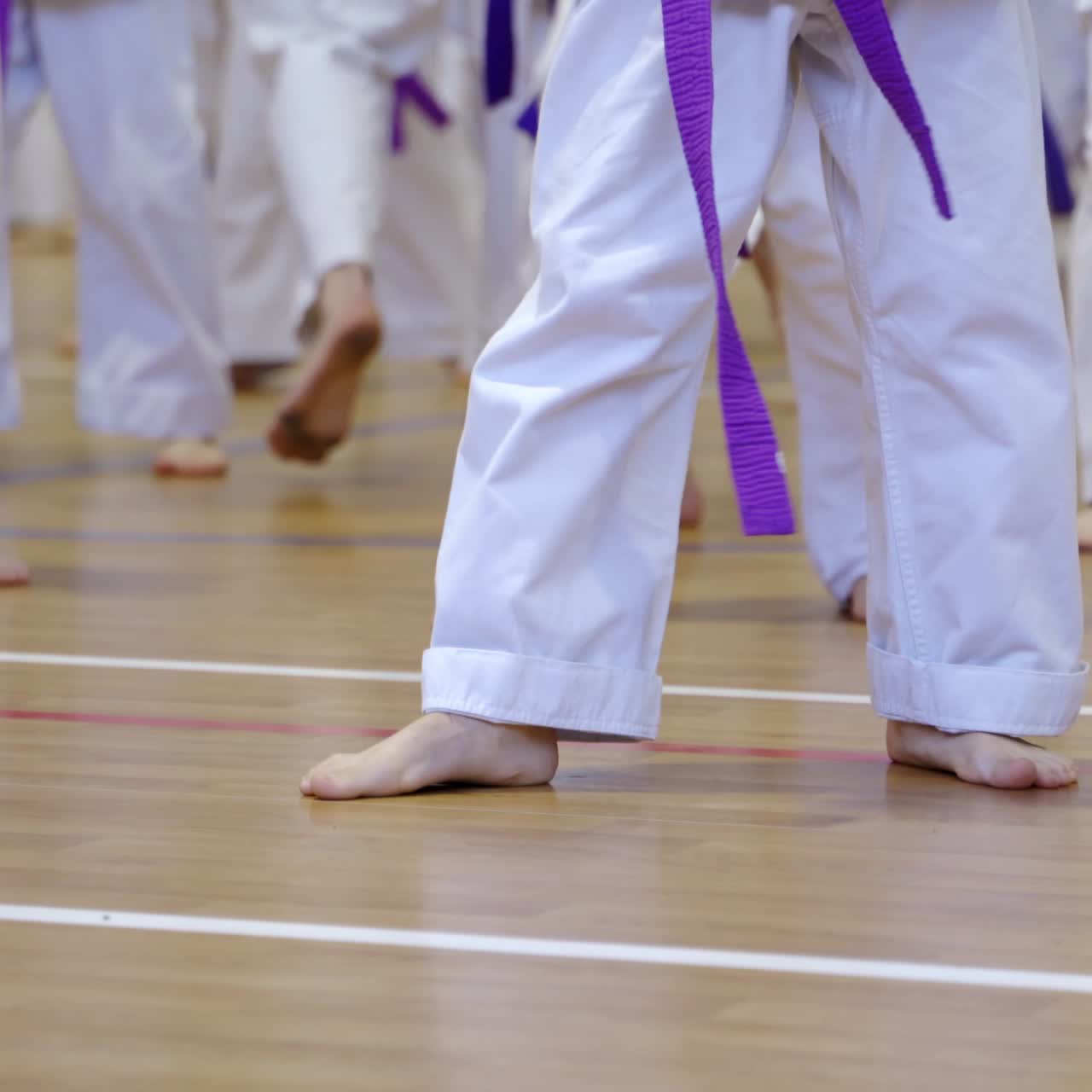 Barefoot practicing kicks at karate training. The legs of young athletes doing exercise standing on wooden floor