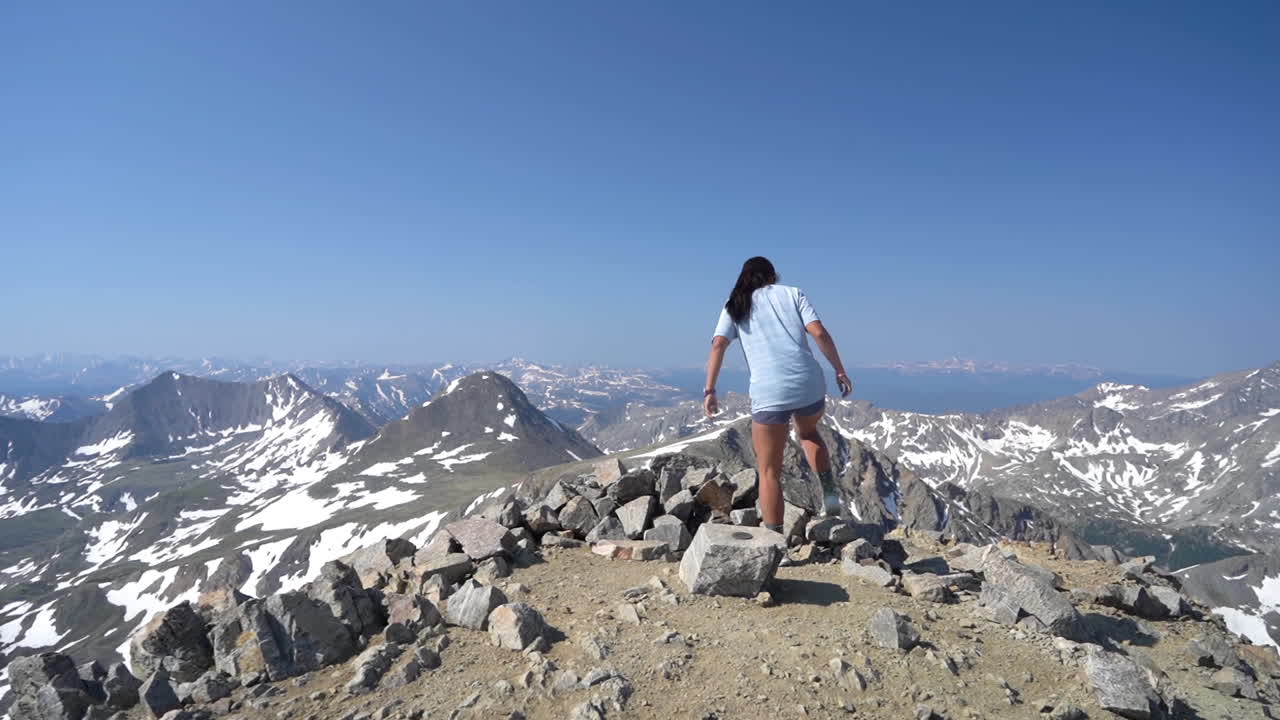 vista trasera de una joven en la cima del pico con impresionantes vistas de la cordillera en un día soleado