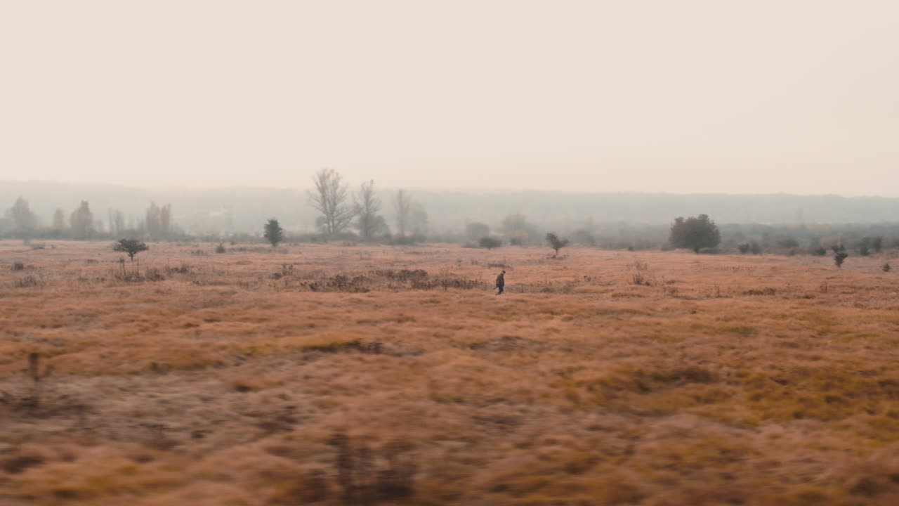 Photographer carrying a camera striding through grassy autumn field