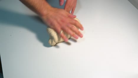 kneading pizza dough by hand on a white table top