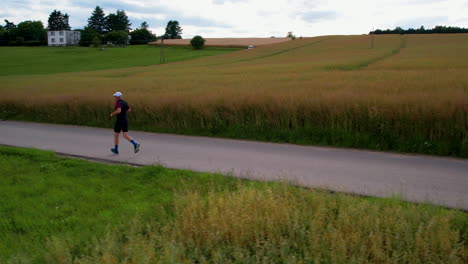 drone shot showing male jogger jogging on path between agricultural fields of poland at sunset - slow motion