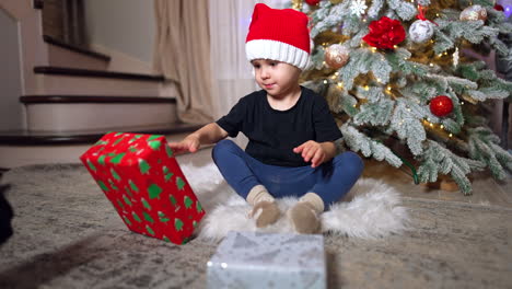 lovely cute caucasian baby is focused on the presents. kid sits on the floor near the christmas tree.