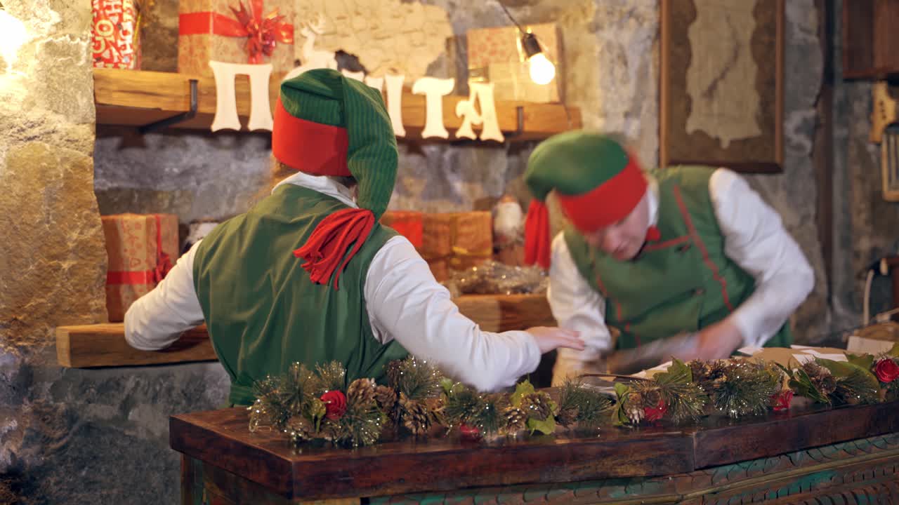 Elves with envelopes. Fairy characters in green costumes with letters at Christmas time. Female elf holding black feather on Christmas gifts background.