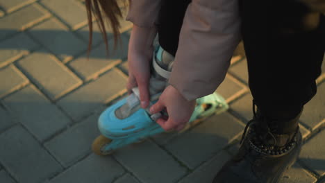 close-up shot of a person sitting in a park, fastening the straps of a light blue rollerblade on one foot while the other leg is still wearing a black boot. moment of preparing for rollerblading