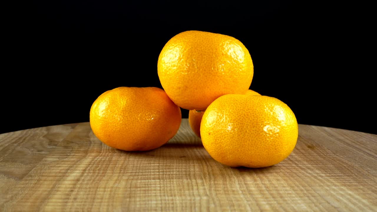 Jeruk mandarin di atas latar belakang hitam. Talenan sedang bergerak