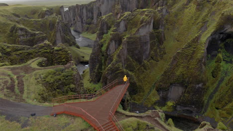 Aerial:-Orbit-shot-of-one-person-with-yellow-jacket-standing-on-the-platform-of-Fjadrargljufur-Canyon-in-Iceland