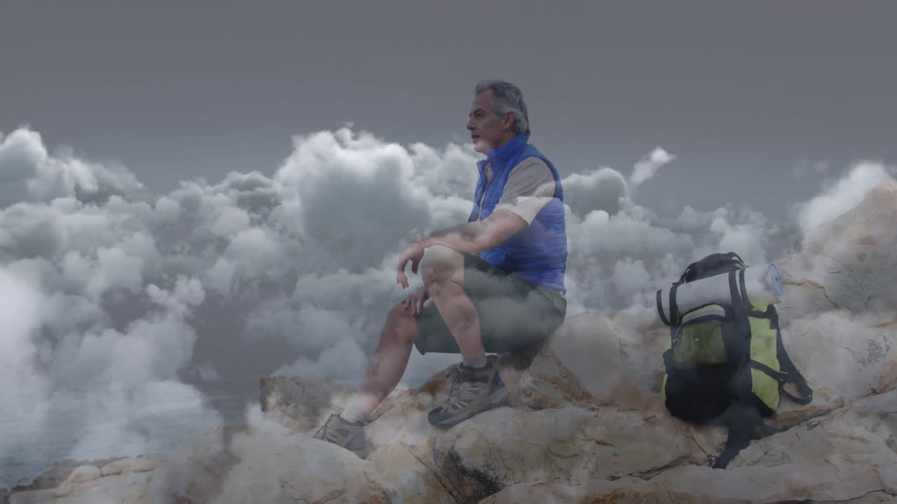 Mature male hiker sitting rocky summit above clouds with backpack, showing business chart overlay
