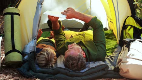 father and daughter using digital tablet outside tent