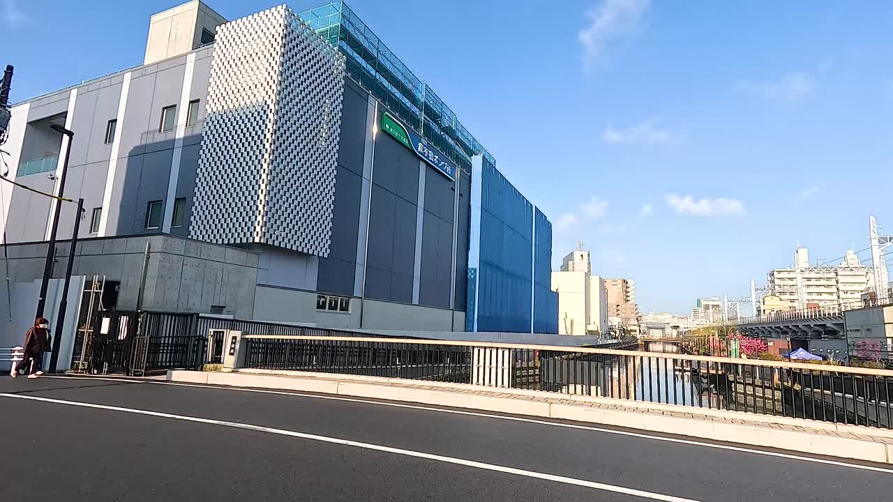 A busy Tokyo street with modern buildings and vehicles passing by under clear blue skies, captured in dynamic motion