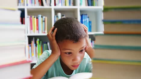 Schoolboy-reading-book-in-library-at-school