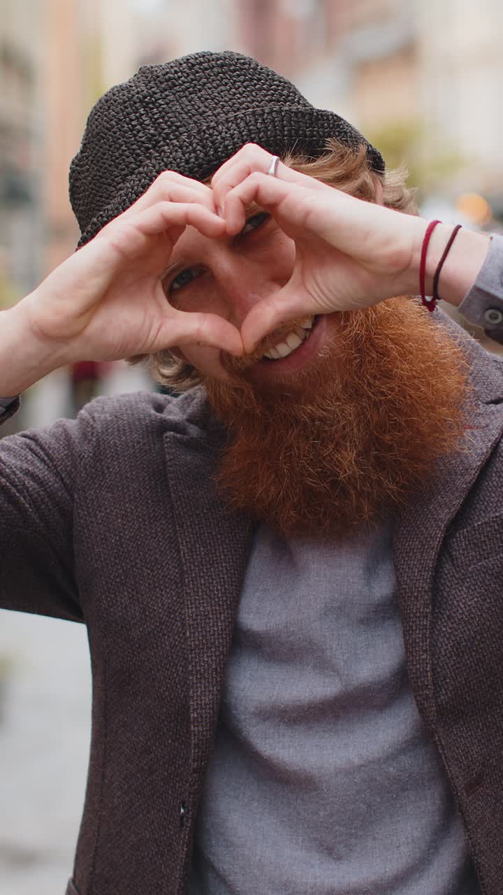 Homem barbudo faz símbolo de amor mostrando sinal de coração para a câmera expressar sentimentos positivos românticos